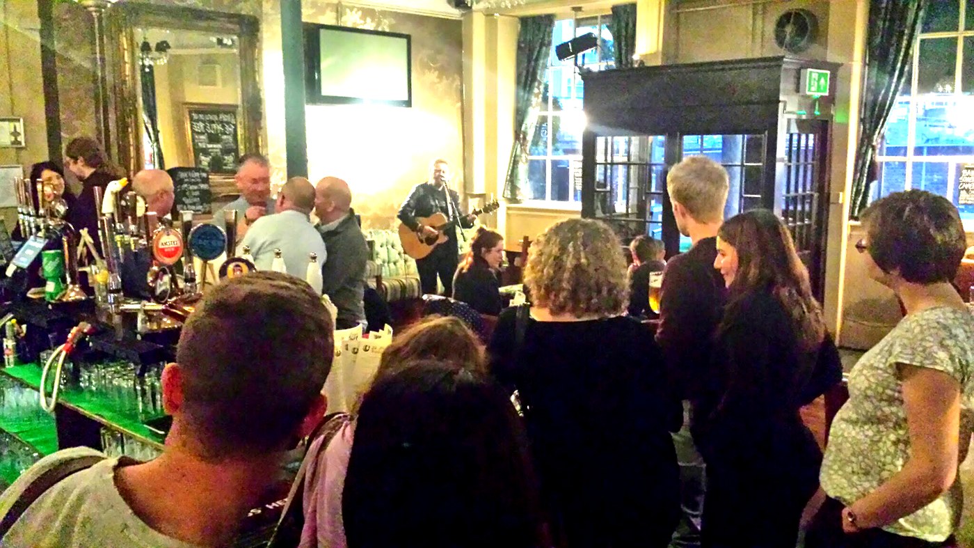 Guitarist performing to a packed crowd in a traditional London pub